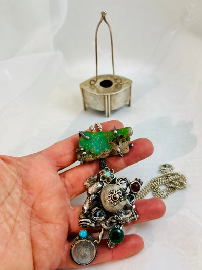 A hand holding one-of-a-kind sacred jewelry pieces in silver and gemstones, crafted with ritual and love in a spiritual artisan studio.